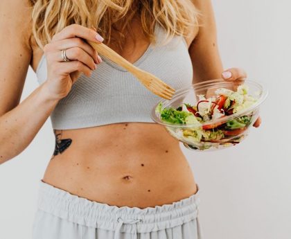 Young woman in sports attire holding a fresh salad bowl, promoting a healthy lifestyle.