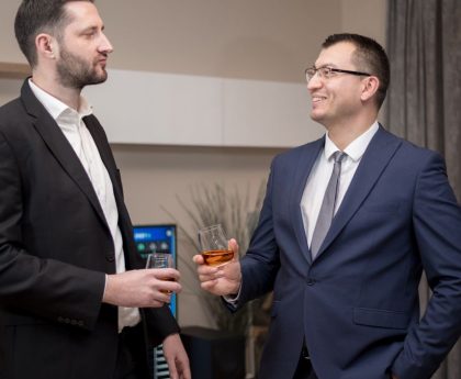 Two business professionals socializing indoors, wearing formal attire, engaging in a friendly conversation.