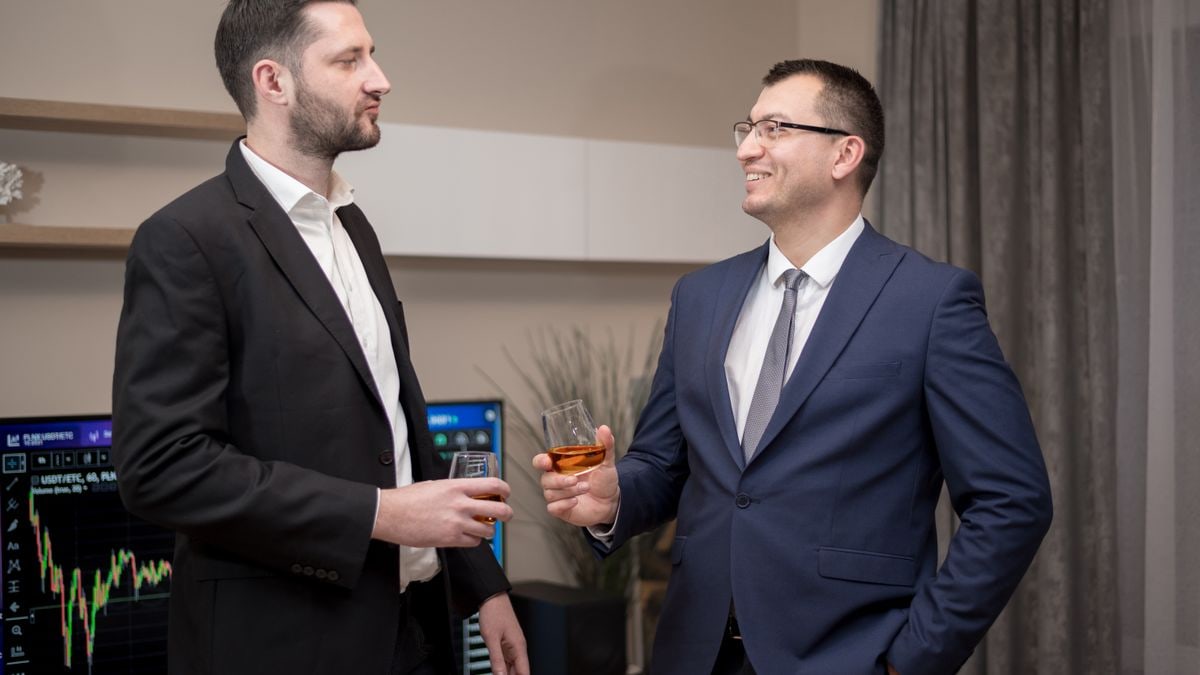 Two business professionals socializing indoors, wearing formal attire, engaging in a friendly conversation.